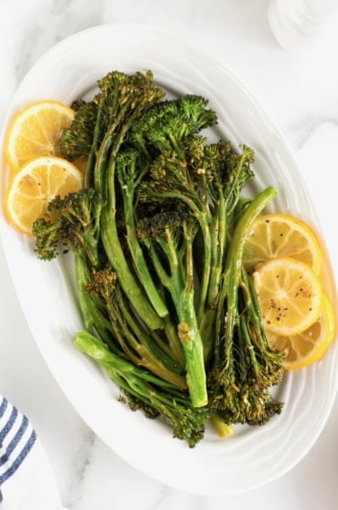 A white oval serving platter of broccolini and lemon slices.