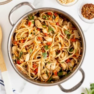 A stainless steel pot of chicken pad Thai on a white marble counter.