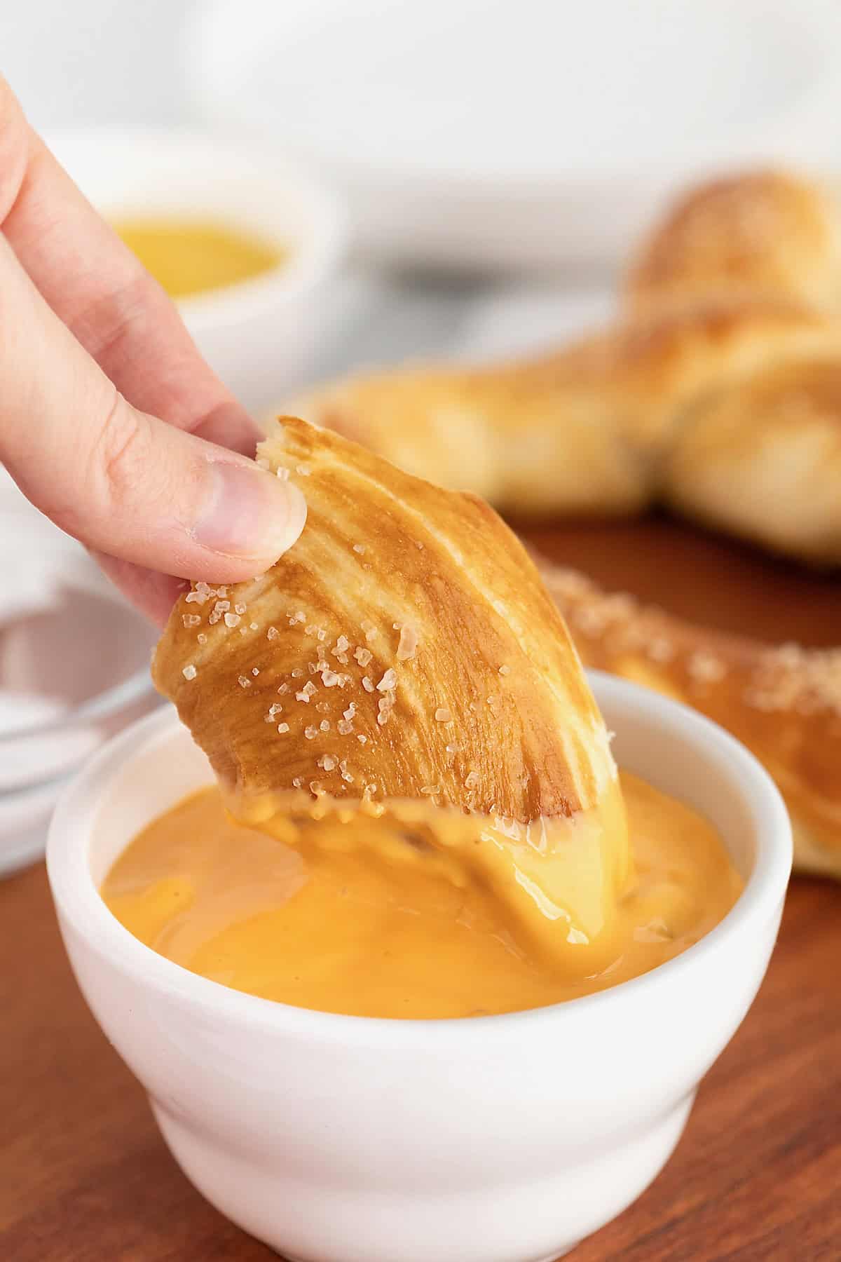 A piece of a jumbo soft pretzel being dipped in cheese sauce.