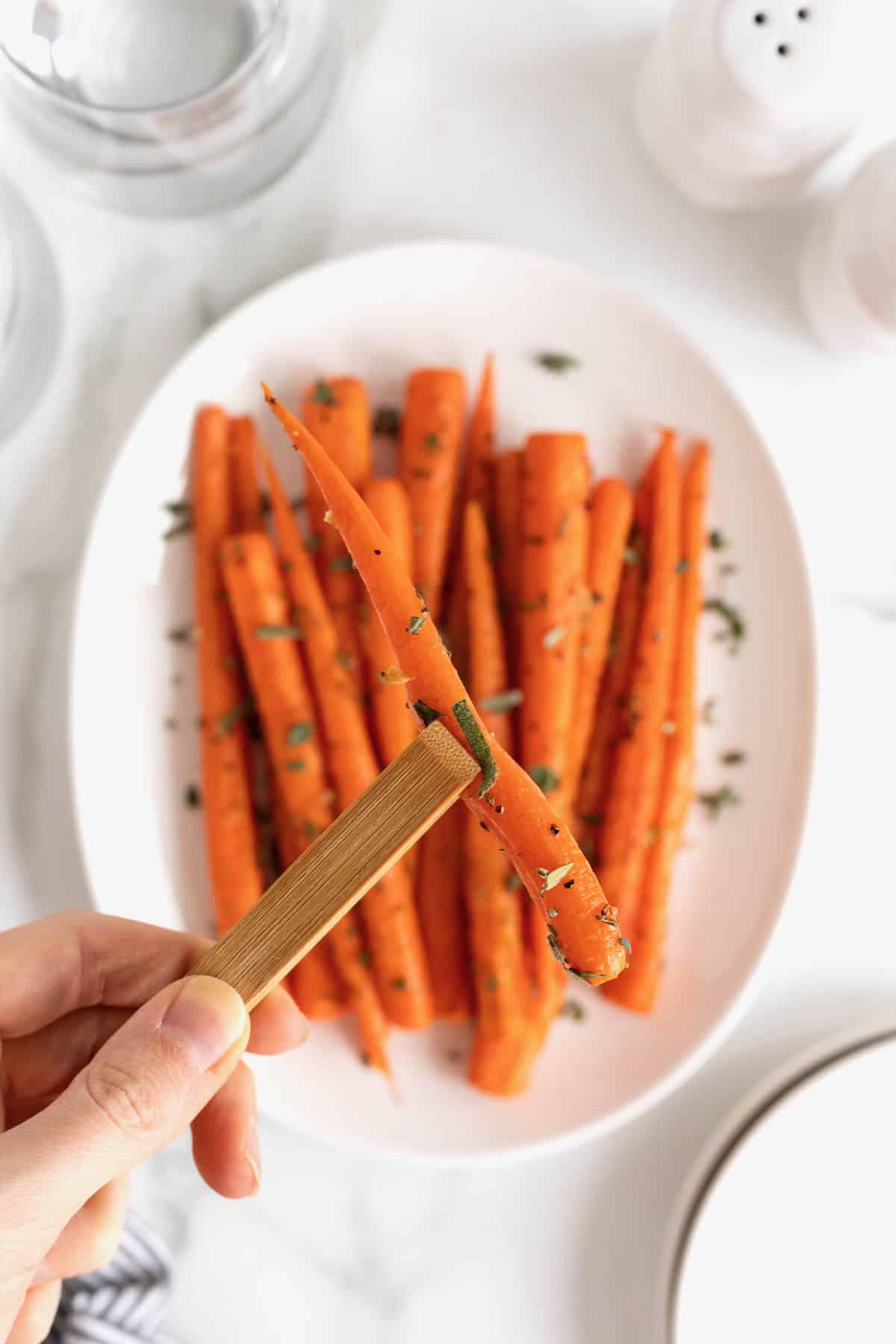 A hand holding a roasted carrot in a pair of wooden tongs.