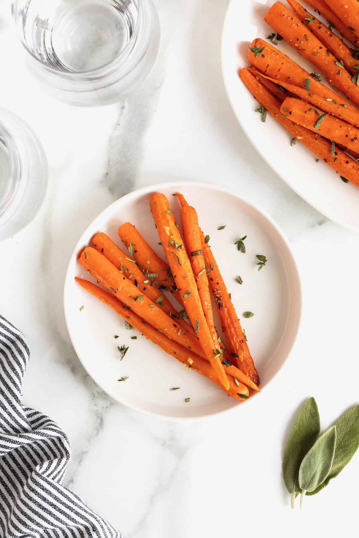 A small white plate of oven roasted carrots garnished with herbs on a white marble counter.