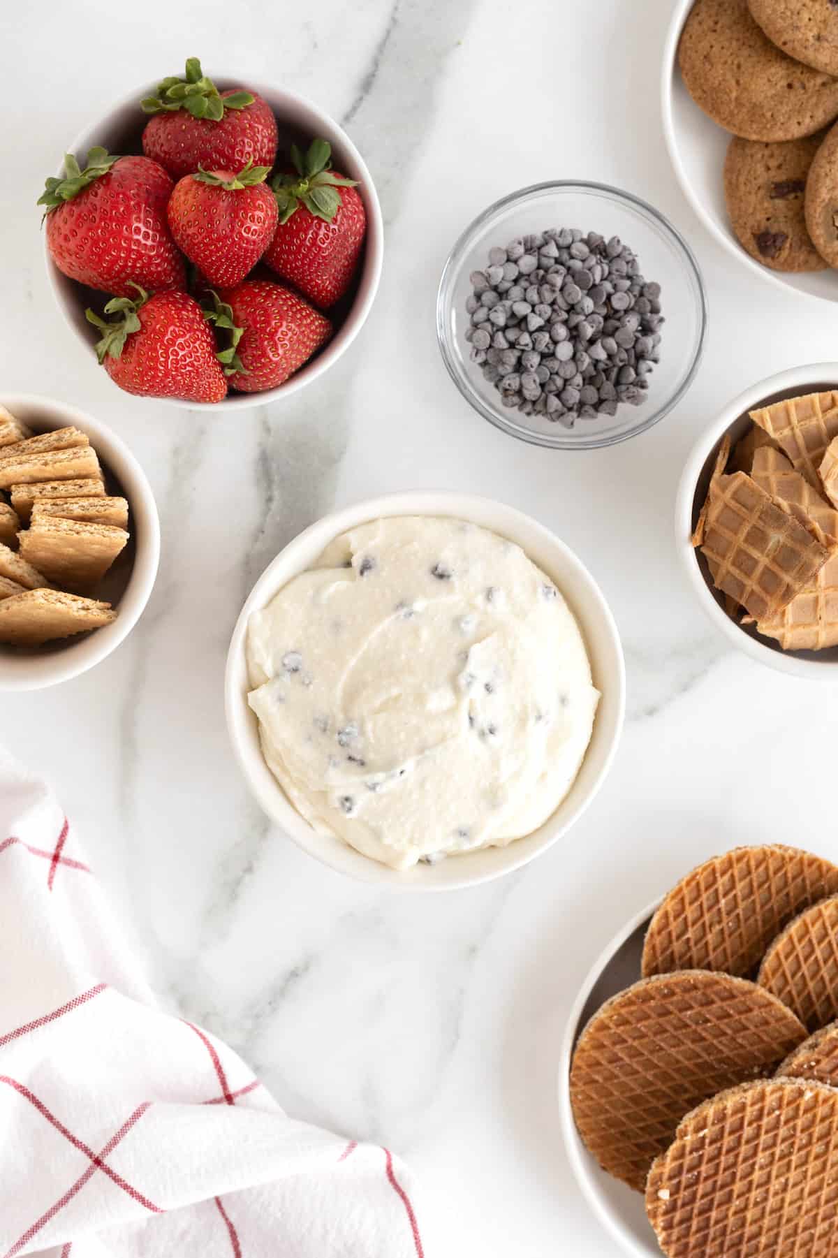 A white bowl of chocolate chip cannoli dip on a white marble counter.