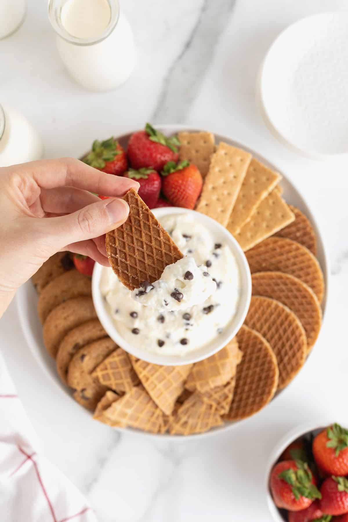 A piece of cookie being dipped into cannoli dip studded with chocolate chips.