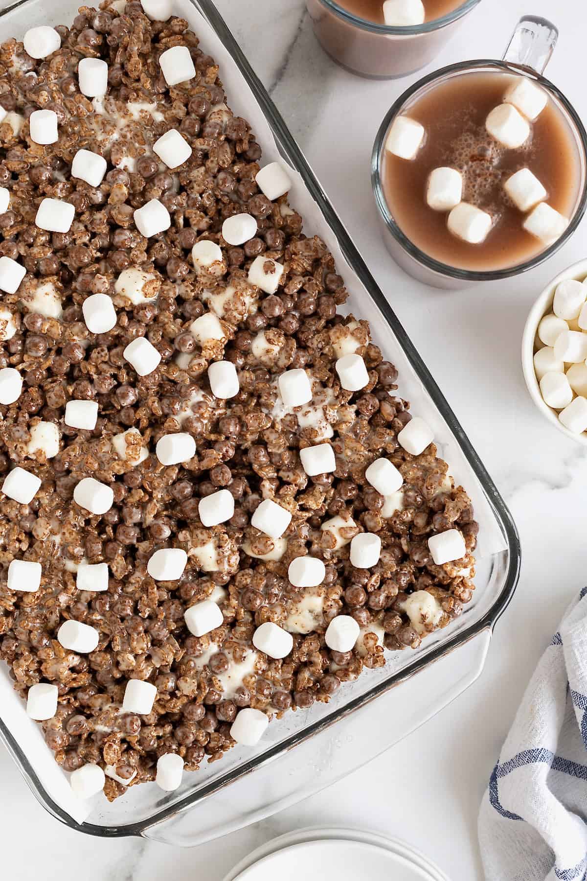 A glass baking dish of hot cocoa Krispie treats on a white marble counter.