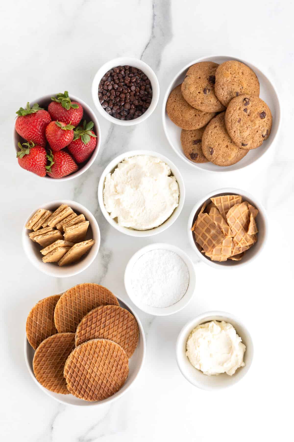 Ingredients to make chocolate chip cannoli dip in small white dishes on a white marble counter.