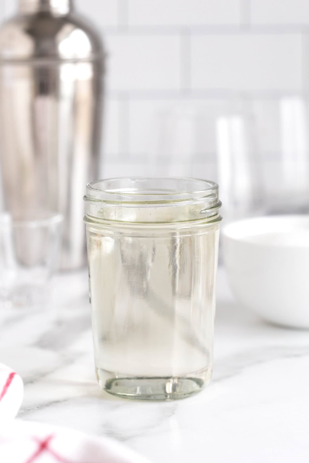 A mason jar containing simple syrup on a white marble counter.