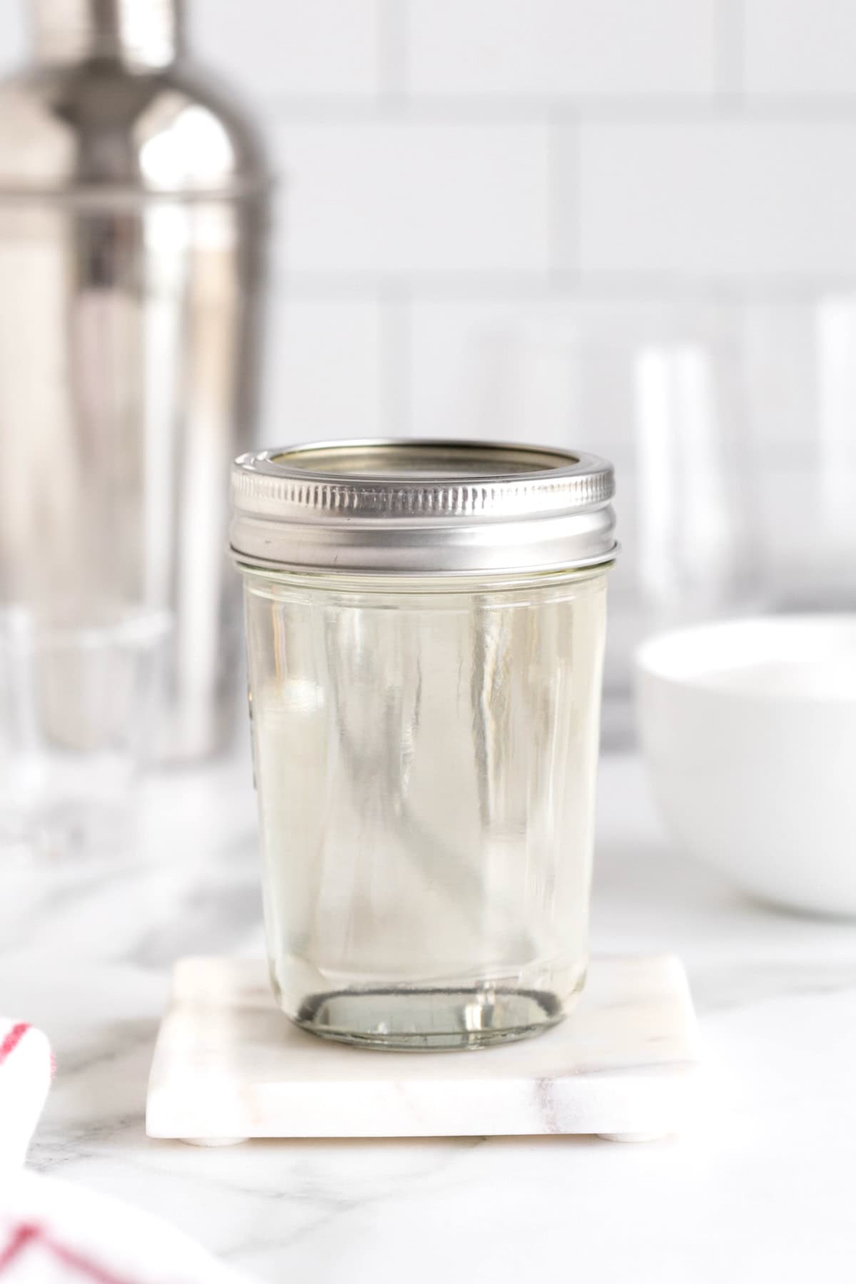 A mason jar with a lid containing simple syrup on a white marble counter.