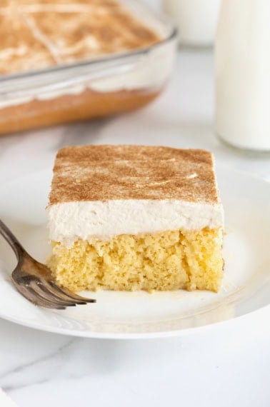 A square of tres leches cake on a white dessert plate with a fork next to it.