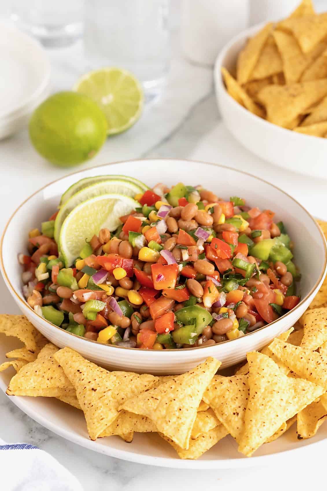 A large gold-rimmed white serving bowl of bean dip with two slices of lime as a garnish.