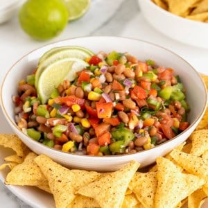 Cowboy Caviar in a white bowl surrounded by corn tortilla chips on a white platter.