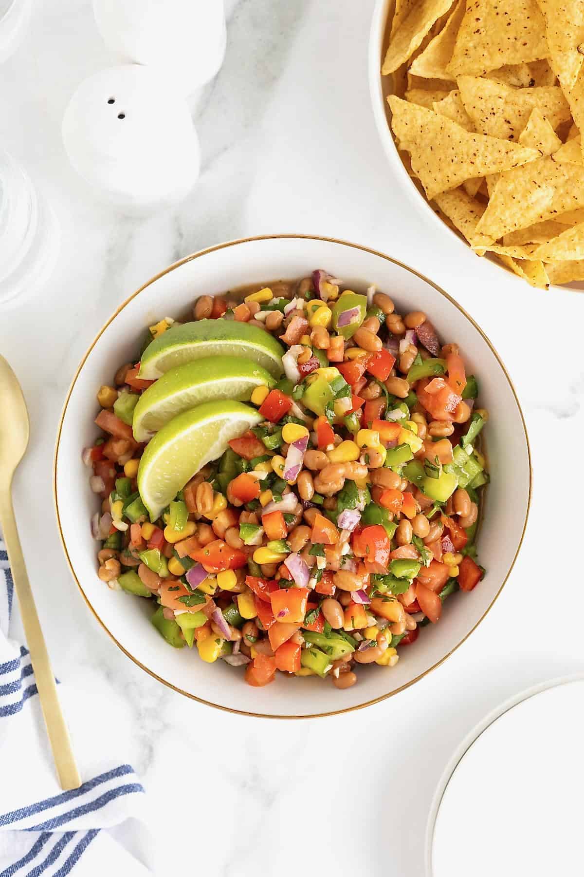A large gold-rimmed white serving bowl of bean dip with two slices of lime as a garnish.
