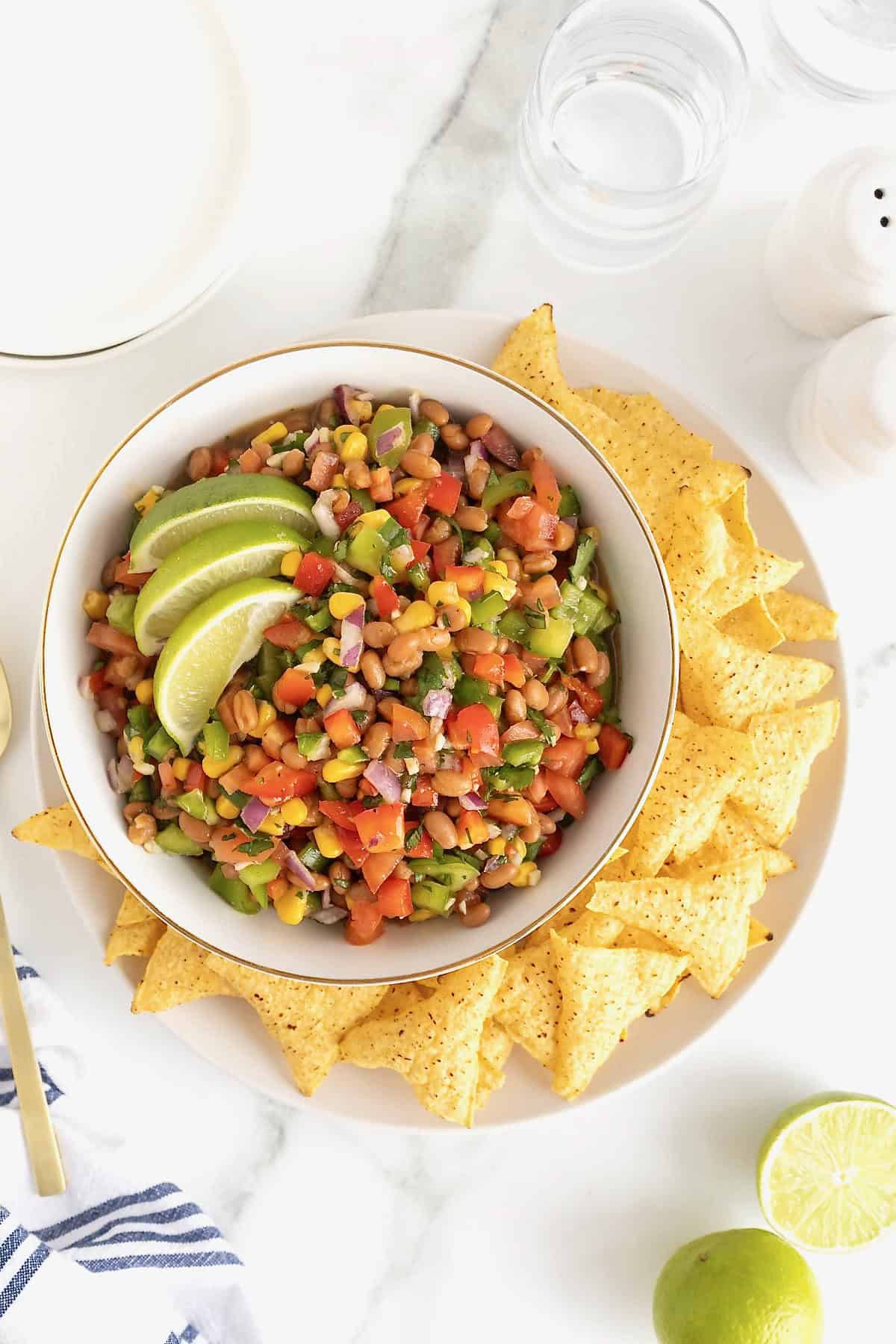 Cowboy Caviar in a white bowl surrounded by corn tortilla chips on a white platter.