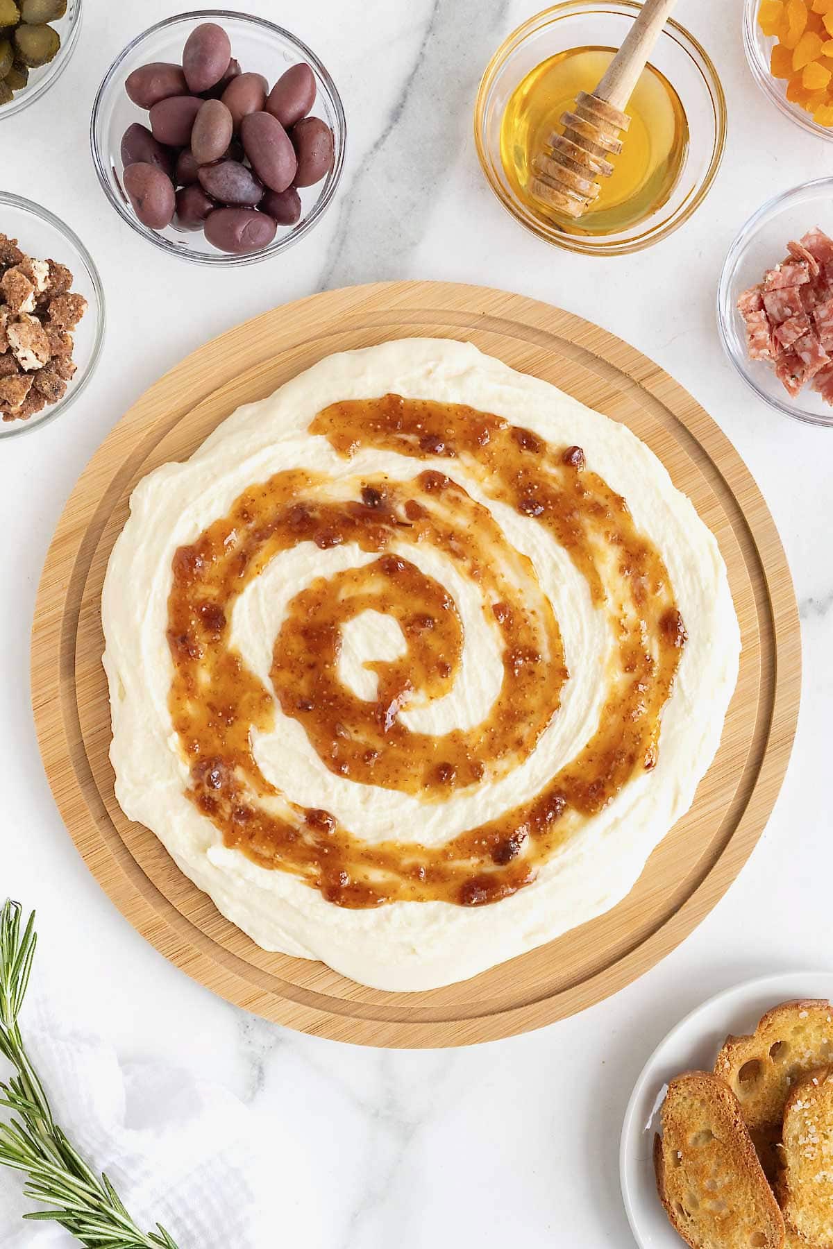 Fig jam swirled on whipped brie on a wooden food board.