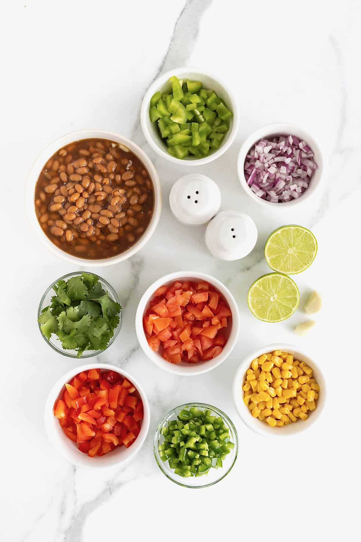 Ingredients for cowboy caviar in small white dishes on a white marble counter.