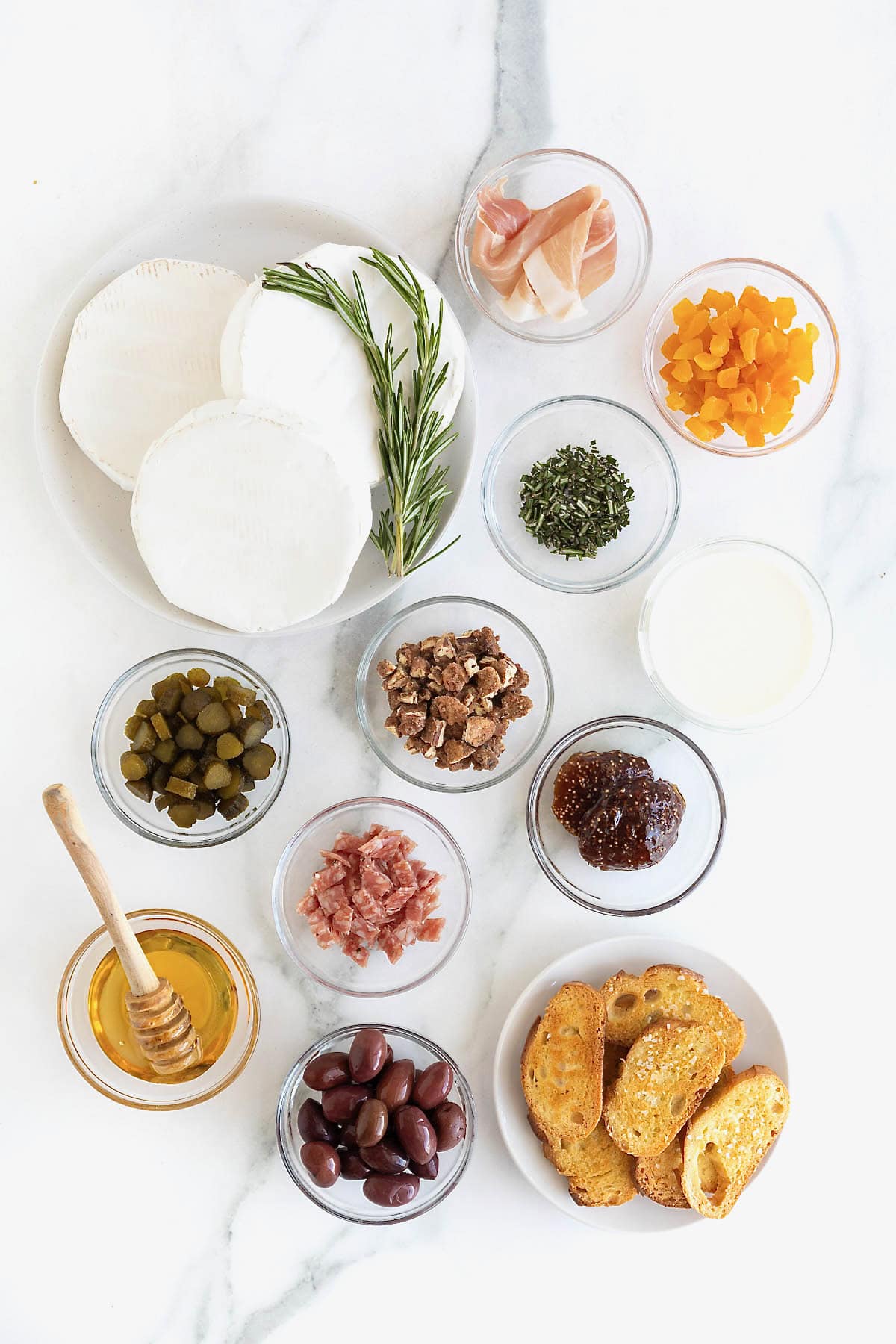 Ingredients to make charcuterie dip in small glass dishes on a white marble counter.