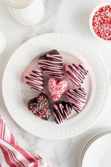 Seven heart-shaped chocolate covered strawberries on a white plate with bead detail.