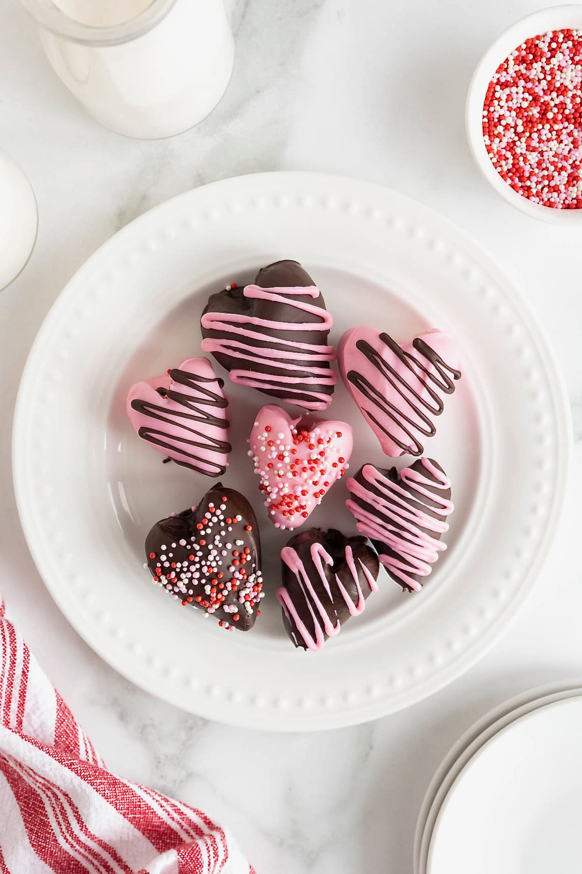 Seven heart-shaped chocolate covered strawberries on a white plate with bead detail.