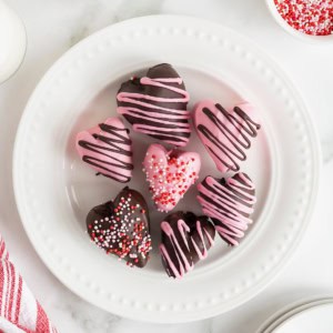 Seven heart-shaped chocolate covered strawberries on a white plate with bead detail.