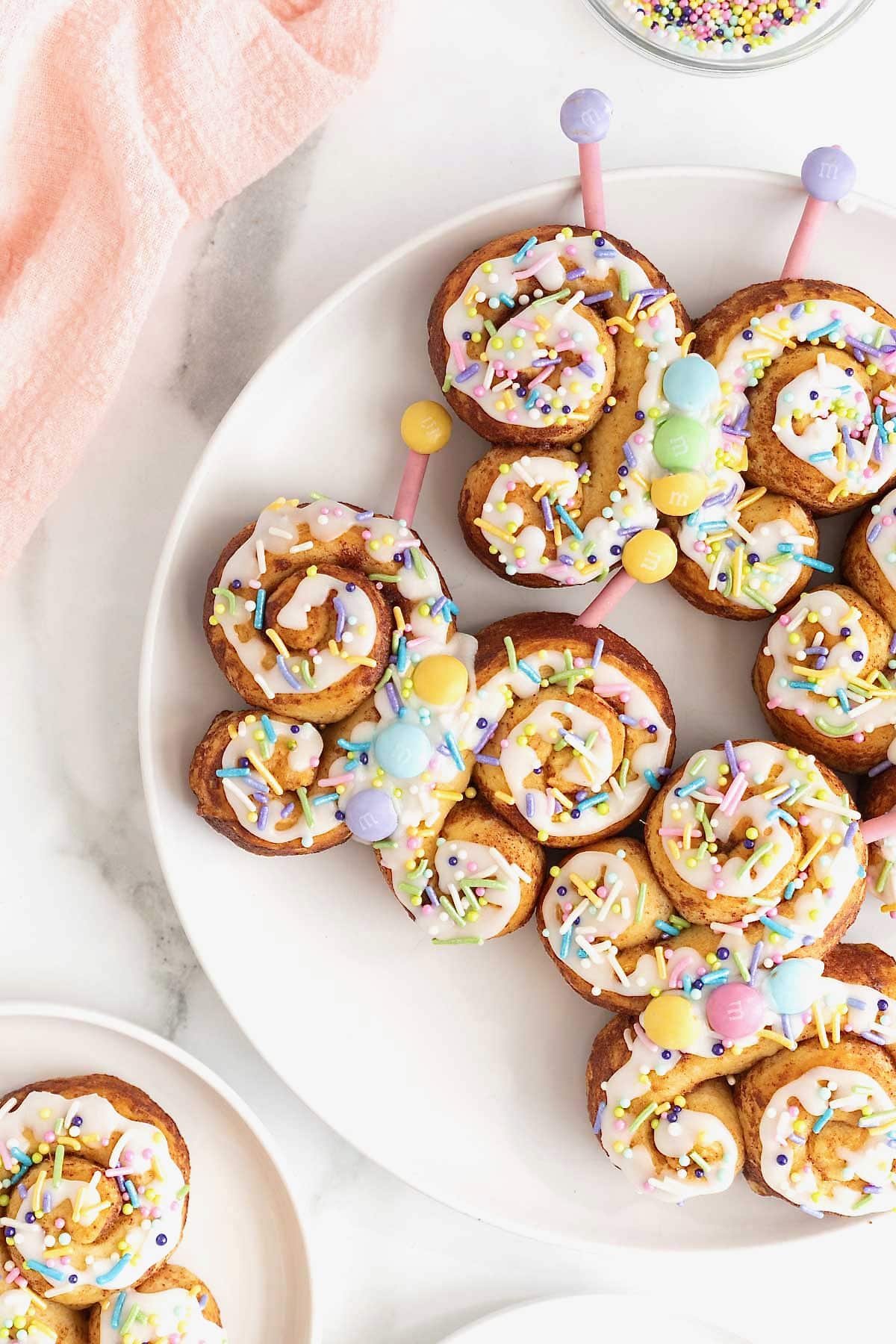 Four butterfly cinnamon rolls decorated with icing and pastel candies on a large white plate.