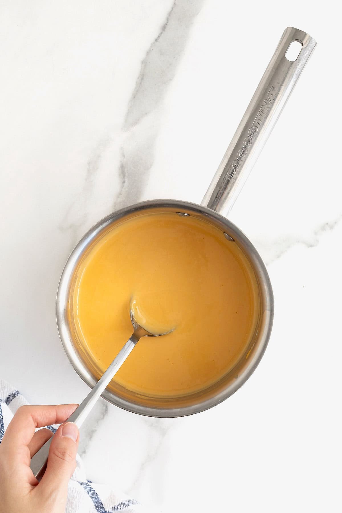 A metal spoon stirring cheese sauce in a metal sauce pan.