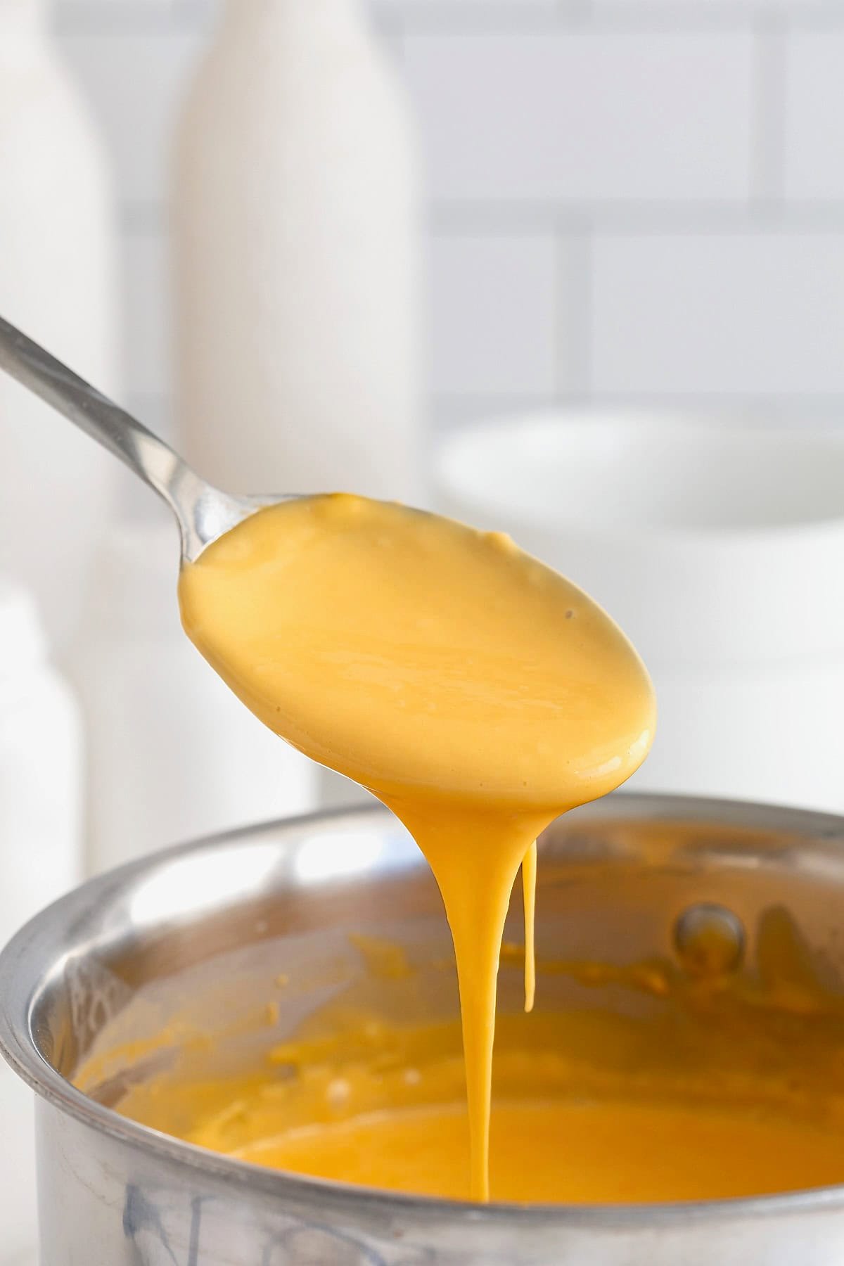 Cheese sauce being poured from a spoon into a stainless steel pot.