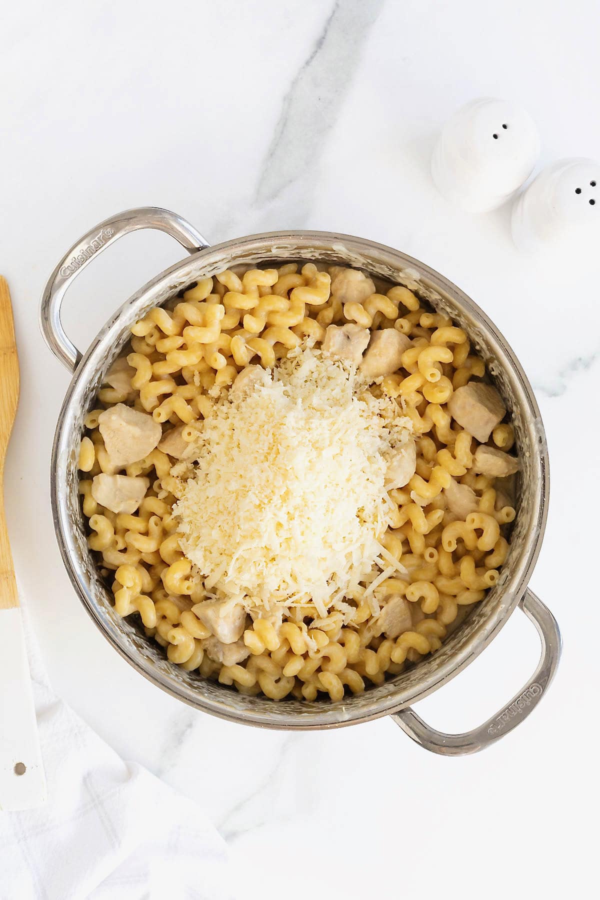 Grated parmesan cheese added to a pot of chicken Alfredo pasta.