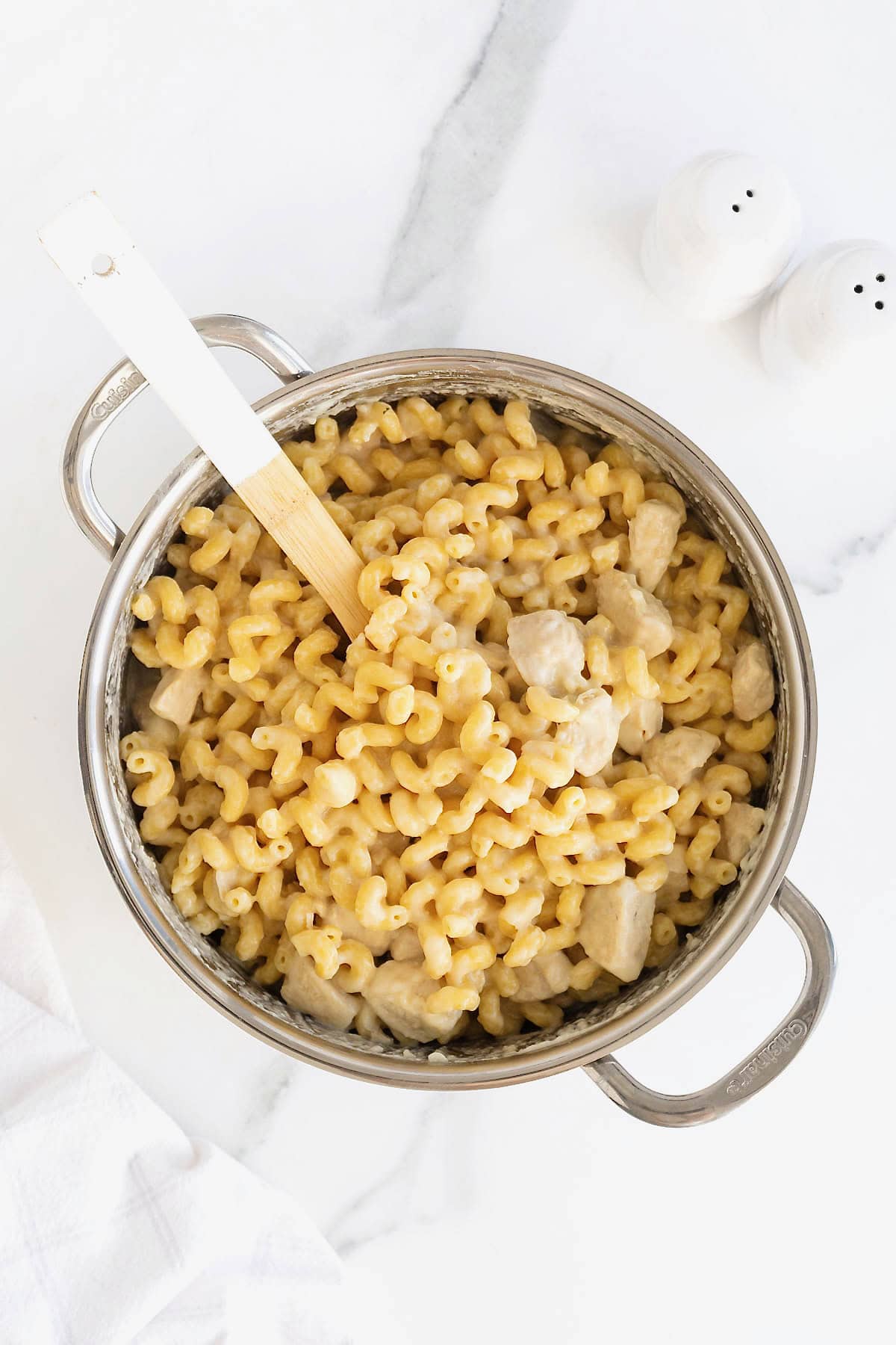 A white handled wooden spoon in a stainless steel pot of chicken Alfredo.