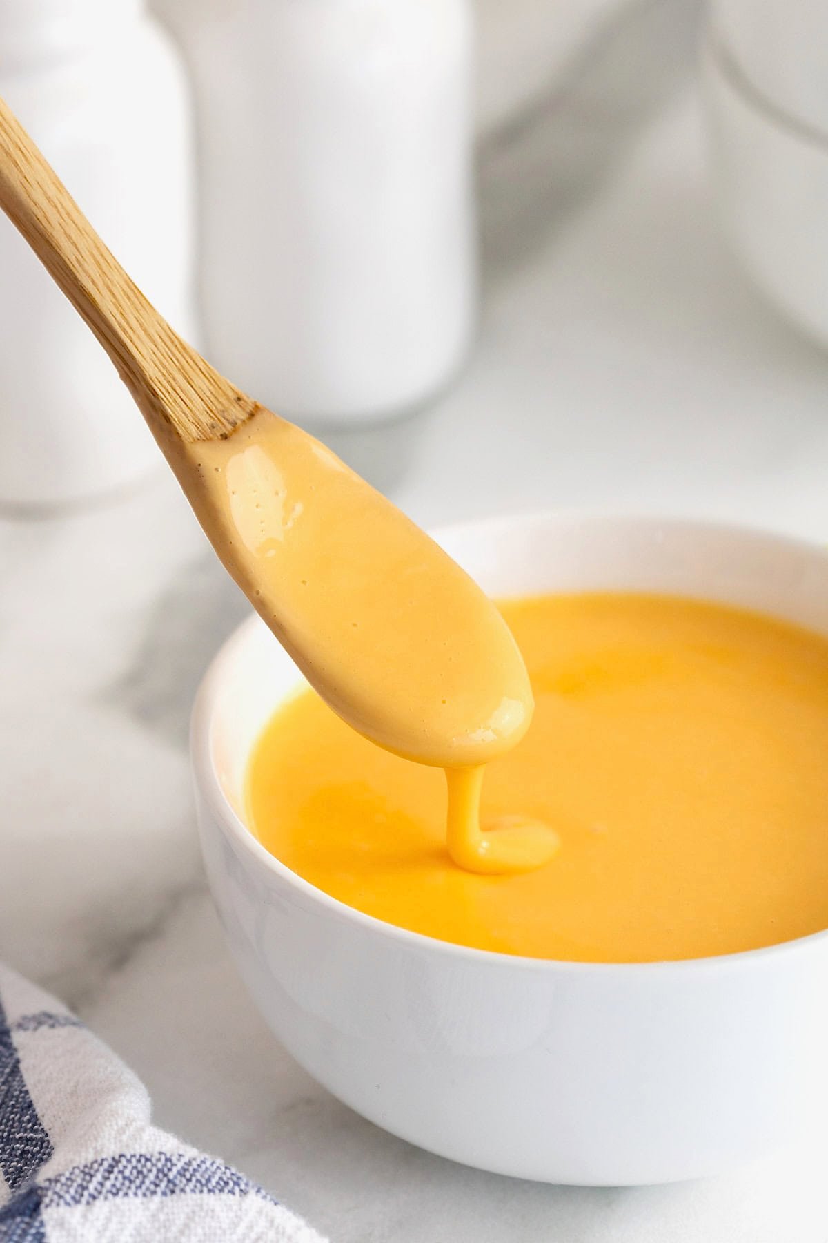 A wooden spoonful of cheese sauce dripping into a white bowl of cheese sauce.