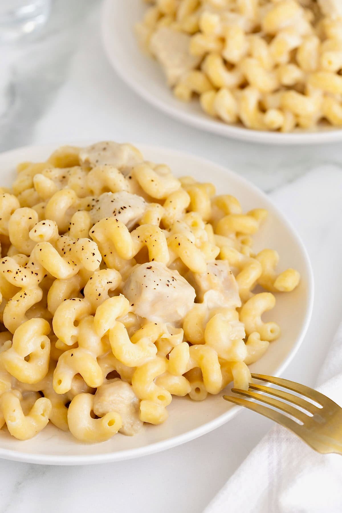 A large white dinner plate filled with cavatappi pasta in a white sauce with chicken.