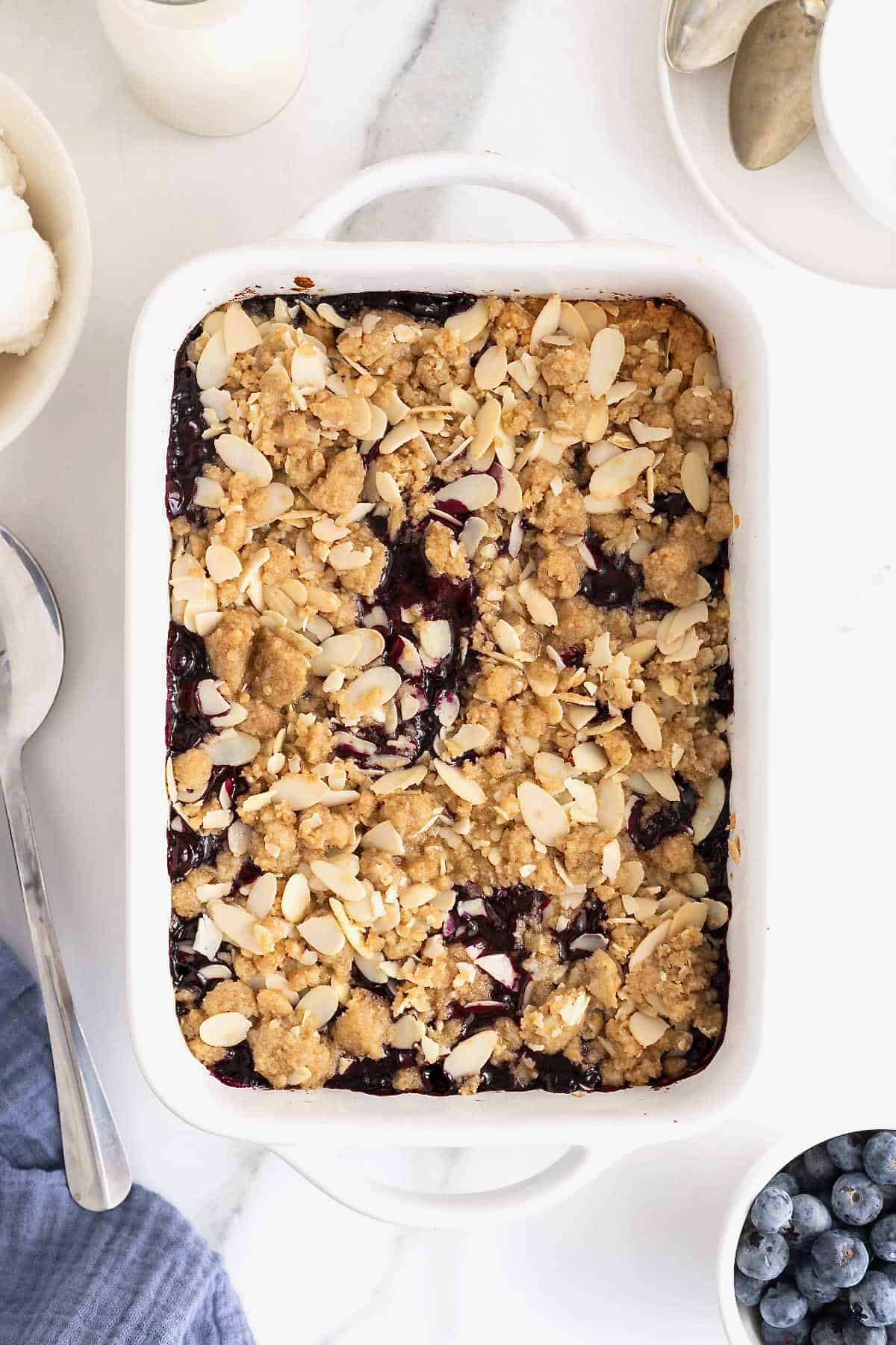 A white baking dish of blueberry almond crisp on a white marble counter.