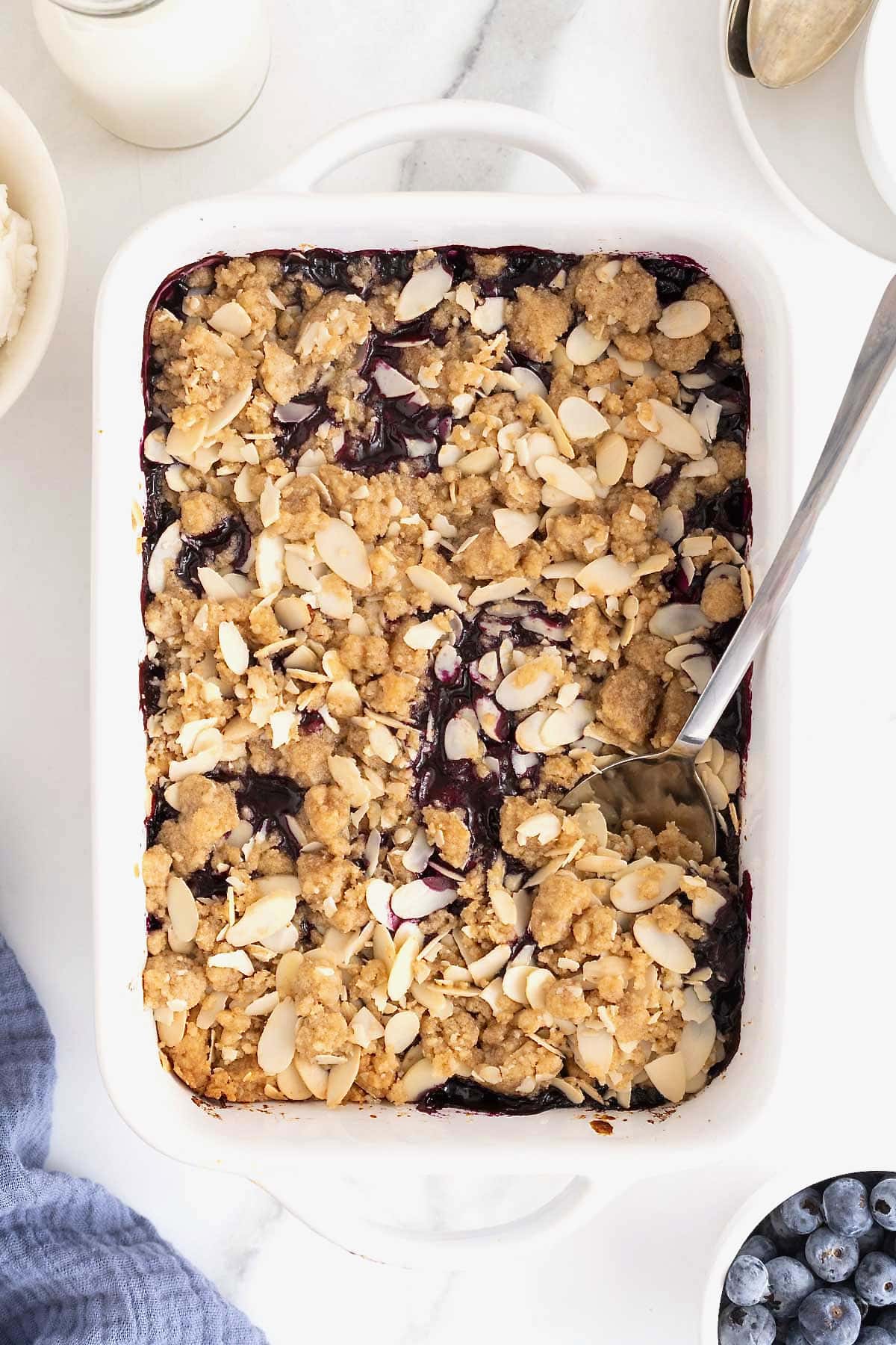 A white baking dish of blueberry almond crisp on a white marble counter.