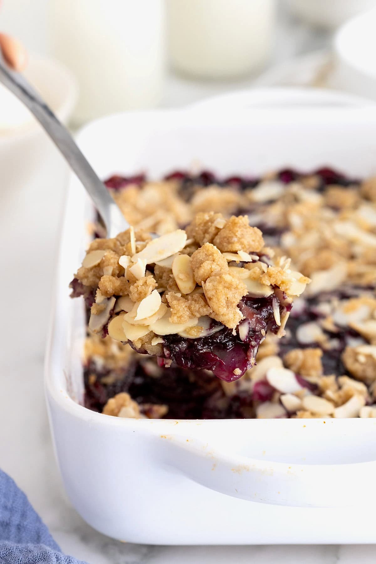 A spoonful of blueberry almond crips being lifted from a small white casserole dish of blueberry crisp