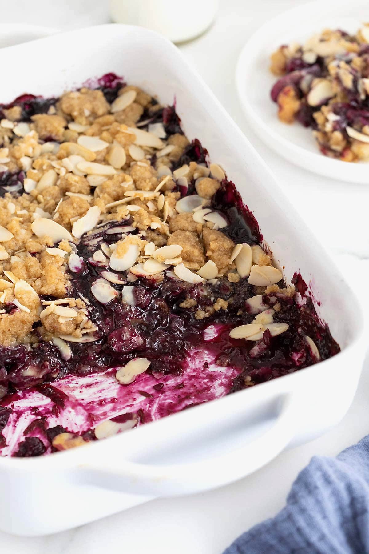 A white baking dish of blueberry almond crisp on a white marble counter.