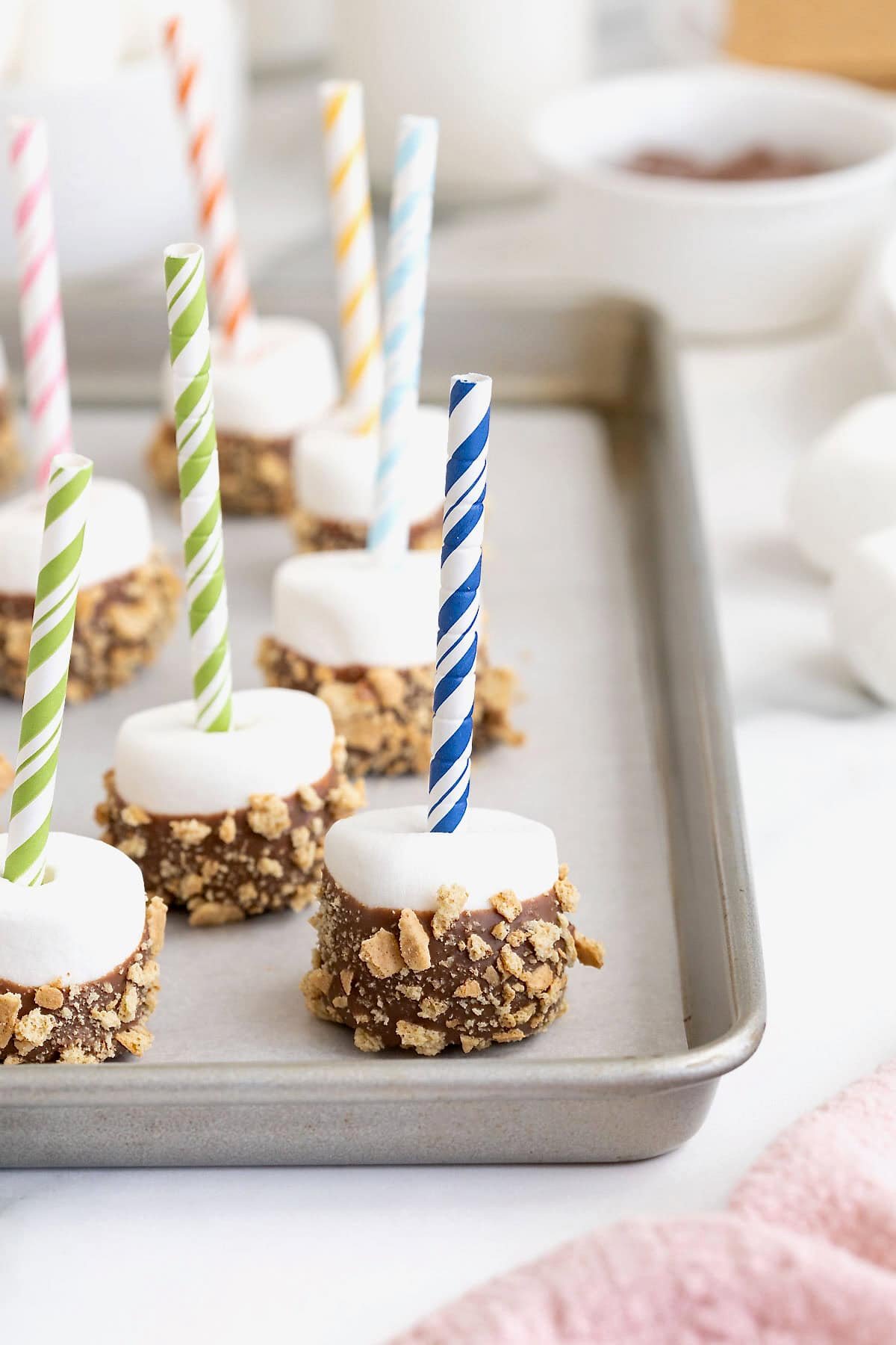 S'mores marshmallow pops on a parchment lined aluminum baking sheet.