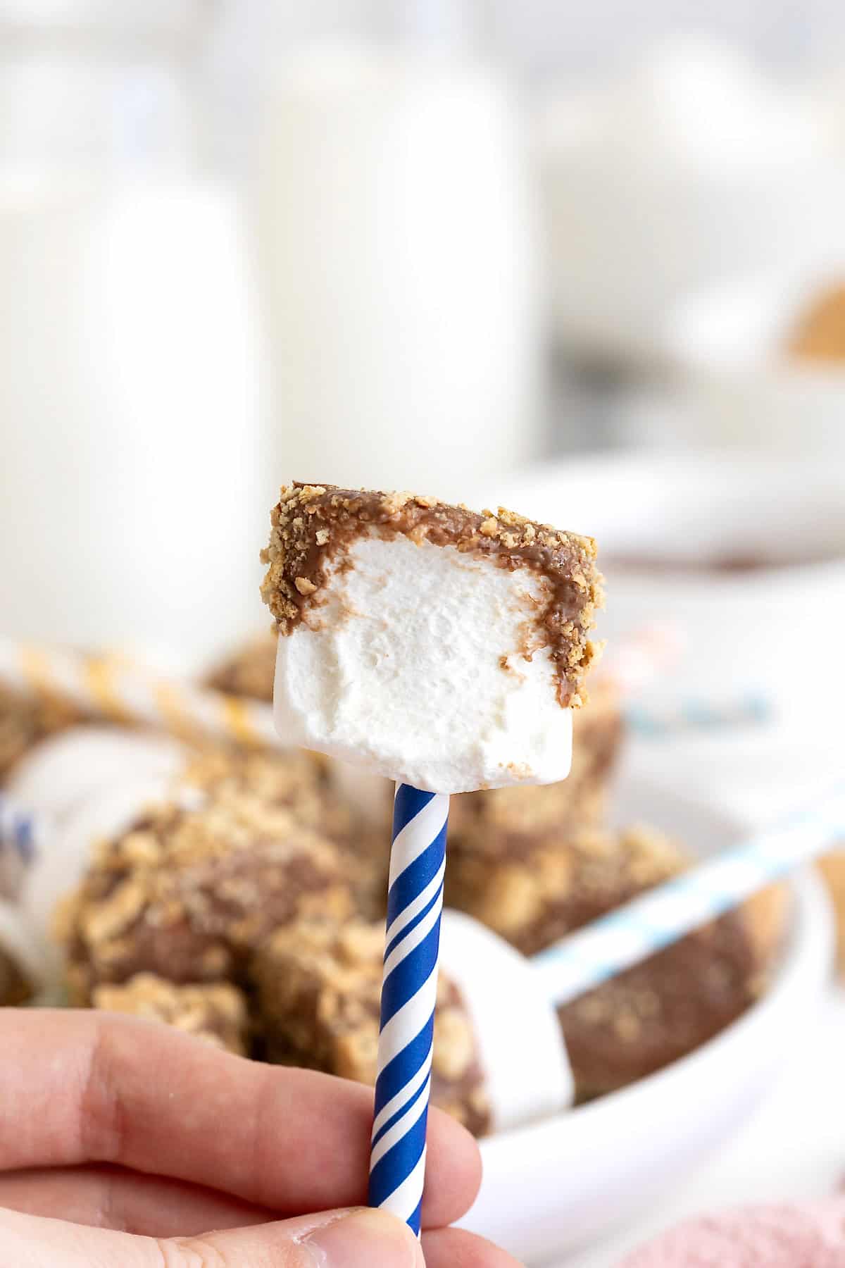 A marshmallow pop on a blue and white striped stick. The marshmallow has a bite out of it.