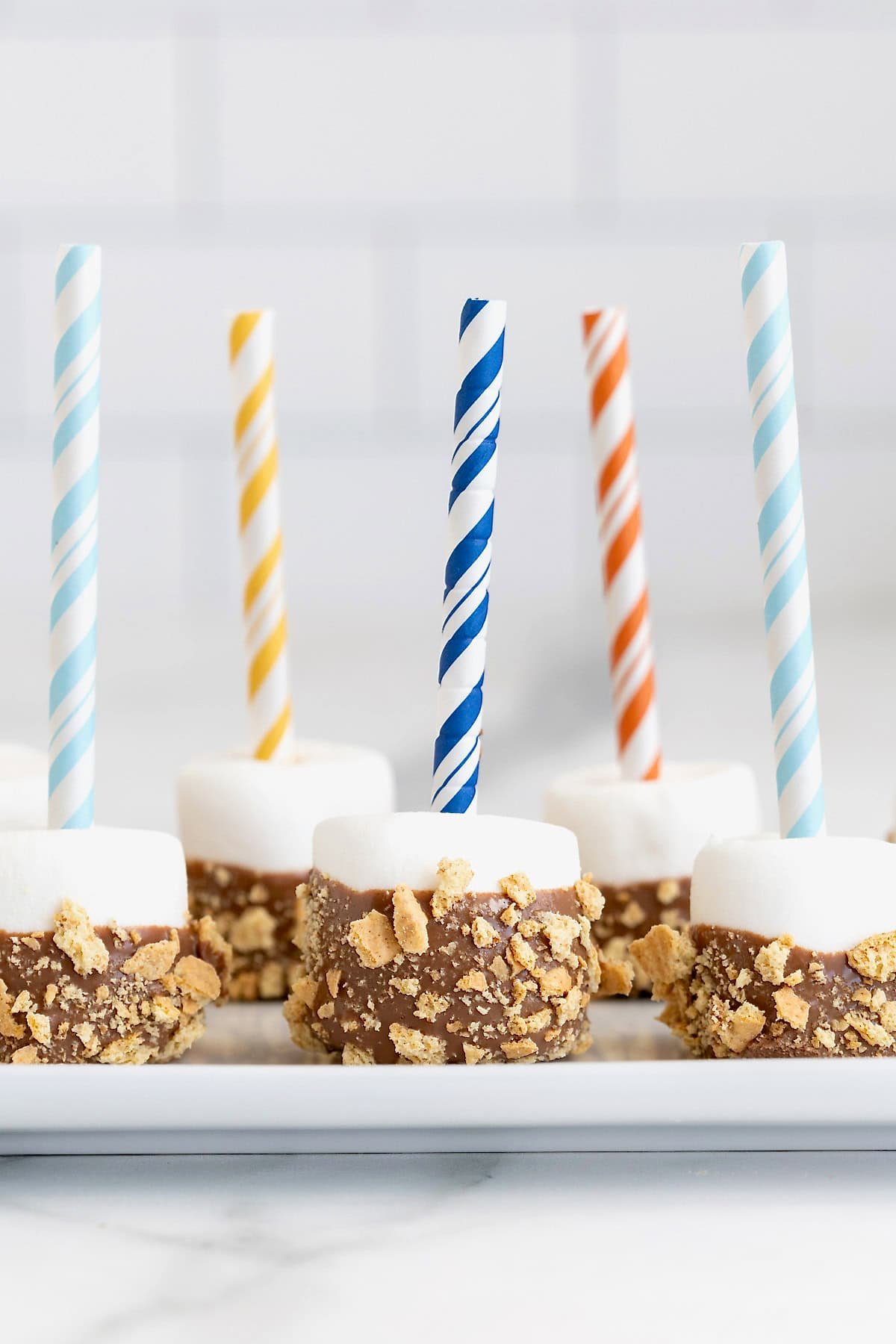 Five s'mores marshmallow pops on a rectangular white plate.