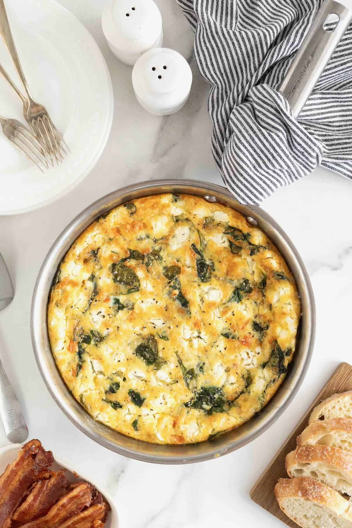 A spinach and goat cheese frittata in a stainless steel pan on a white marble counter.