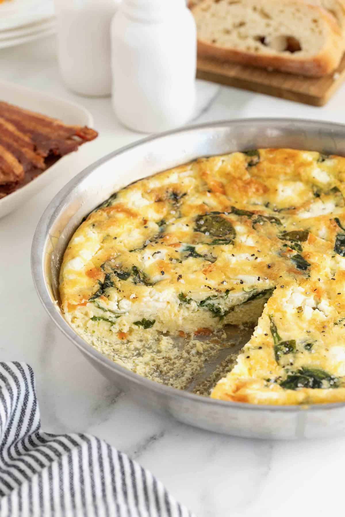 A spinach and goat cheese frittata in an aluminum pan on a white marble counter.