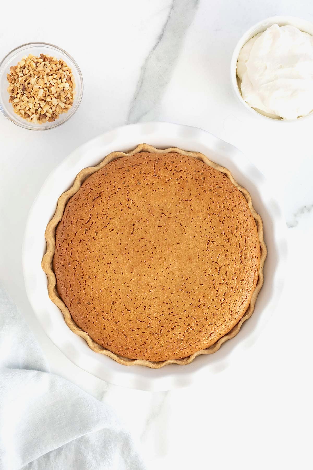 A baked peanut butter pie with a fluted curst in a white fluted pie plate.
