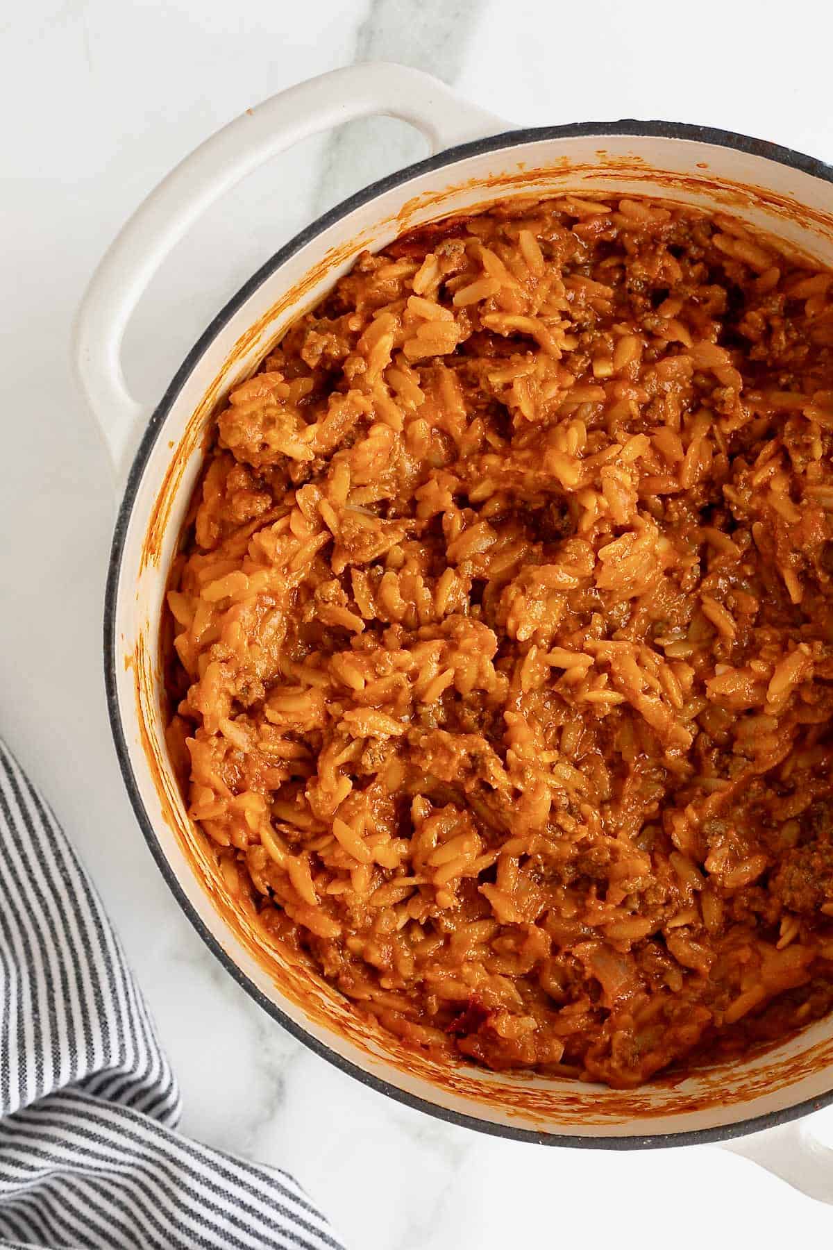 A white Dutch oven of sloppy Joe orzo on a white marble counter.
