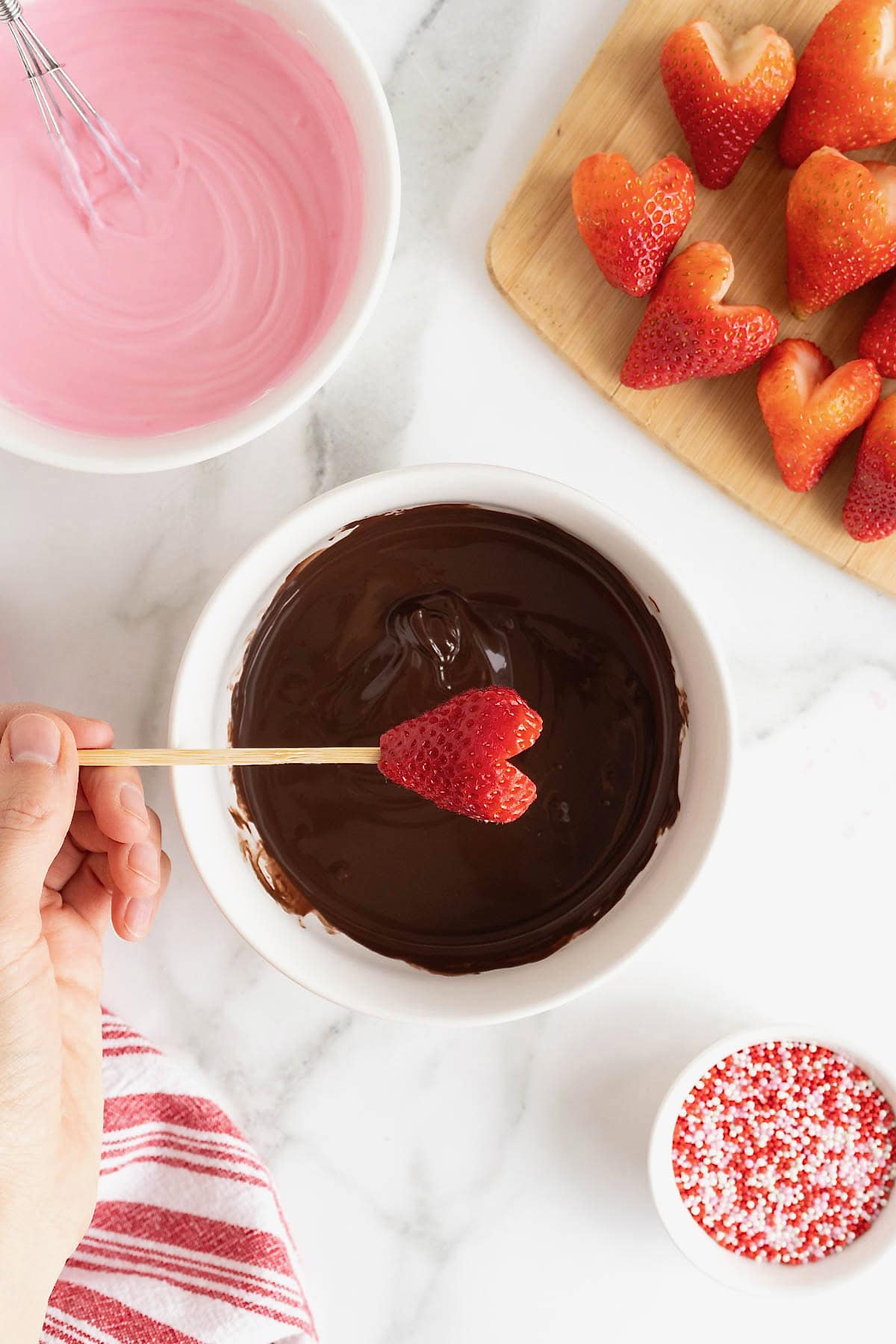 A heart-shaped strawberry being dipped in chocolate.