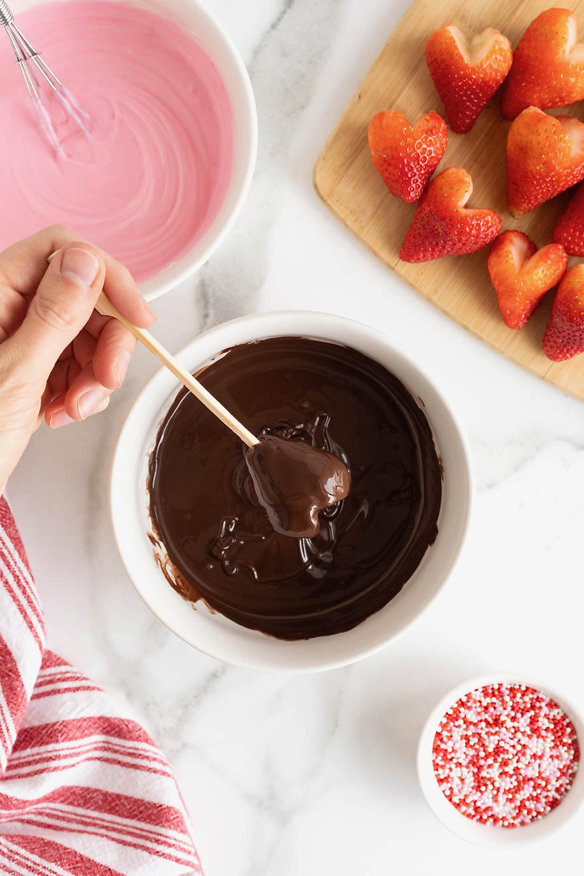 A heart-shaped strawberry being dipped in chocolate.