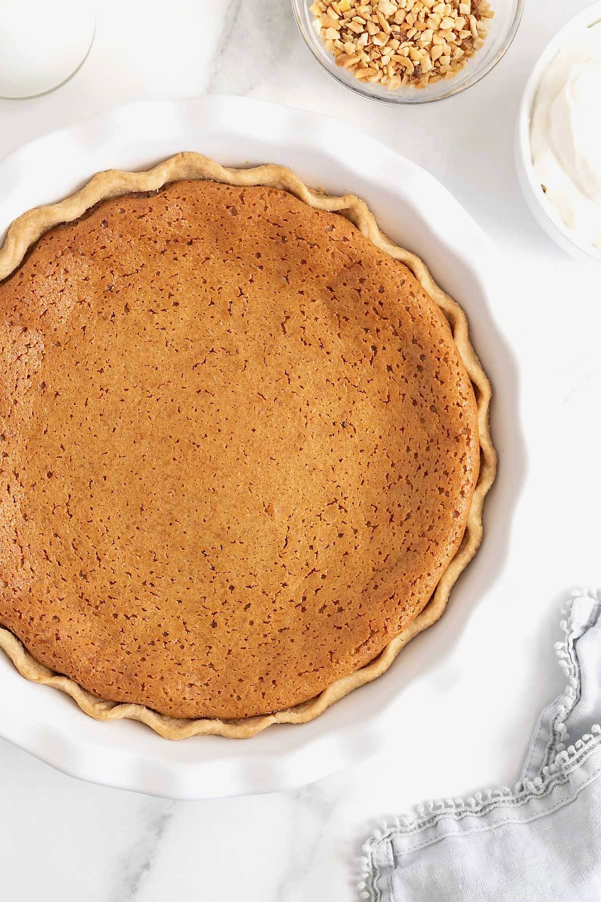 A baked peanut butter pie with a fluted curst in a white fluted pie plate.