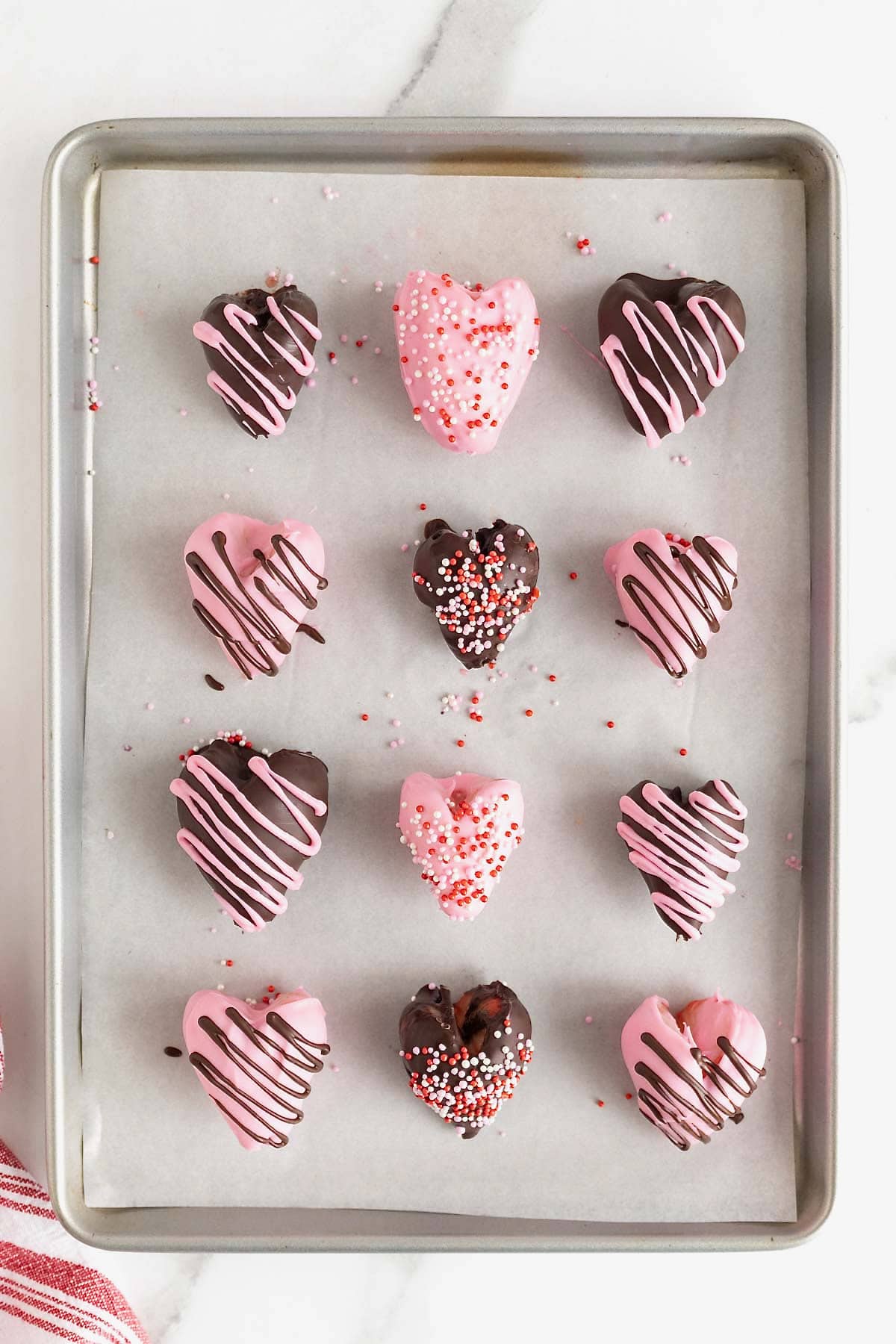 Chocolate covered heart-shaped strawberries on a parchment lined aluminum baking sheet.