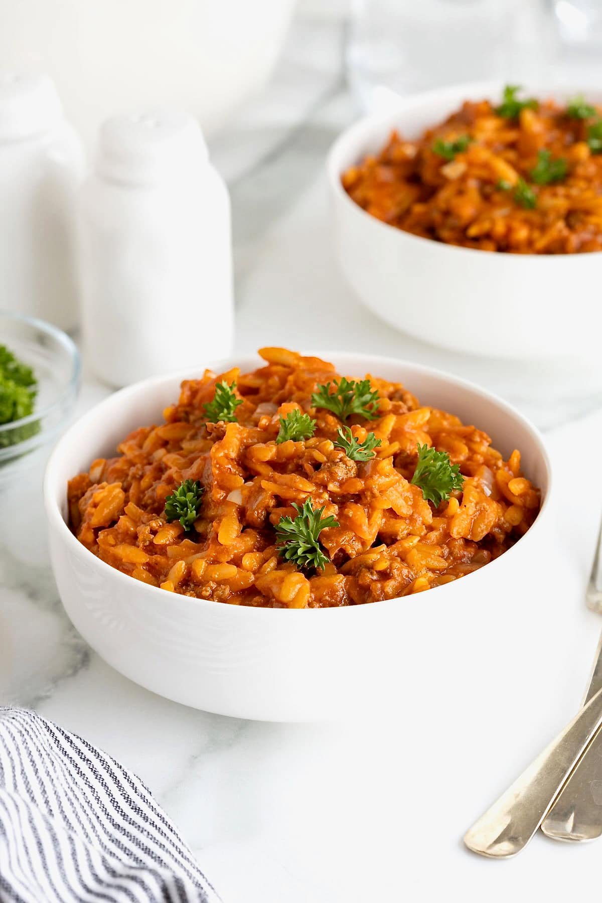 A small white bowl of sloppy Joe orzo on a white marble counter.