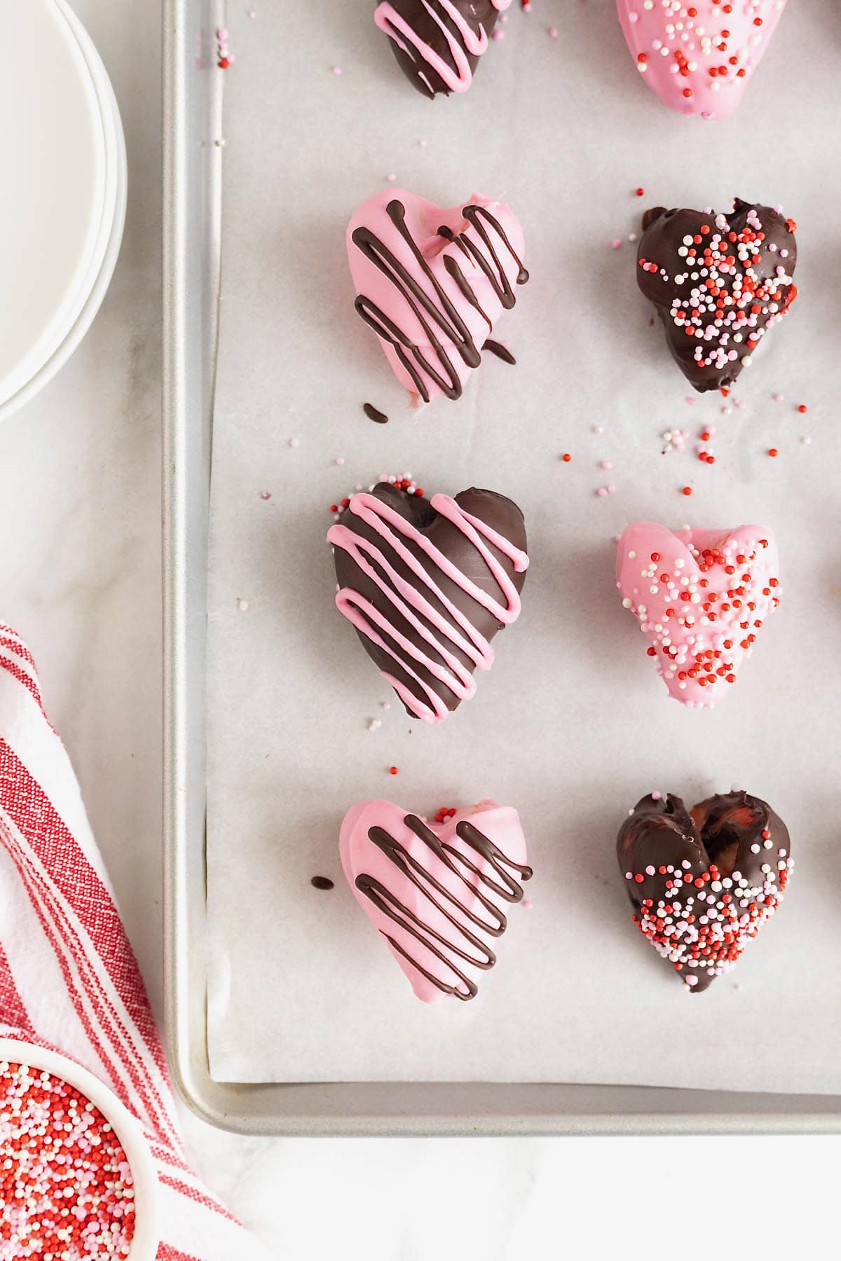 Chocolate covered heart-shaped strawberries on a parchment lined aluminum baking sheet.