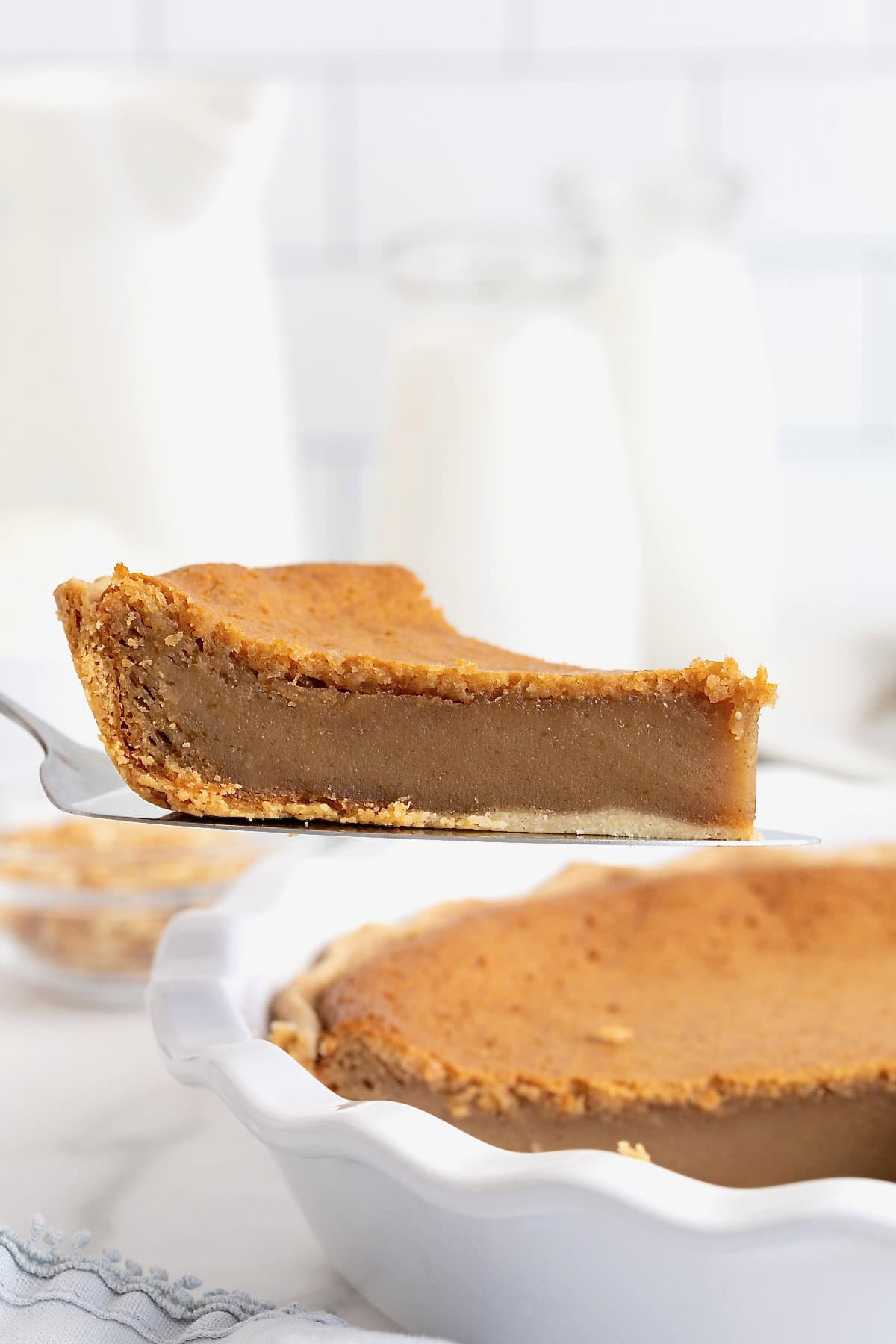 A slice of peanut butter pie being lifted from a white glass pie plate on a metal spatula.