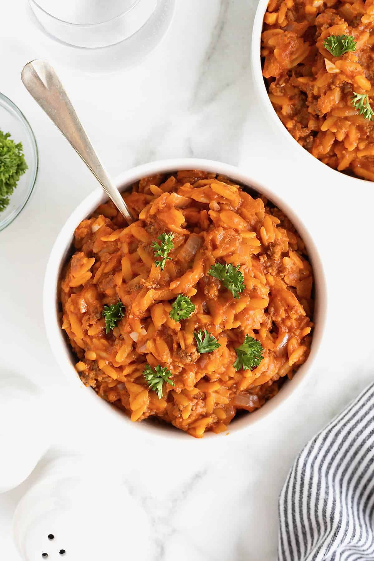 A small white bowl of sloppy Joe orzo on a white marble counter.