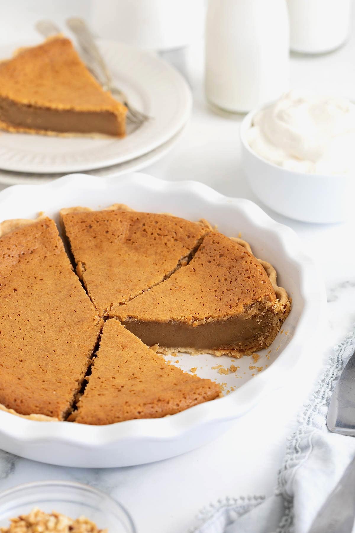A baked peanut butter pie with a fluted curst in a white fluted pie plate. The pie is cut into slices and one slice is missing.