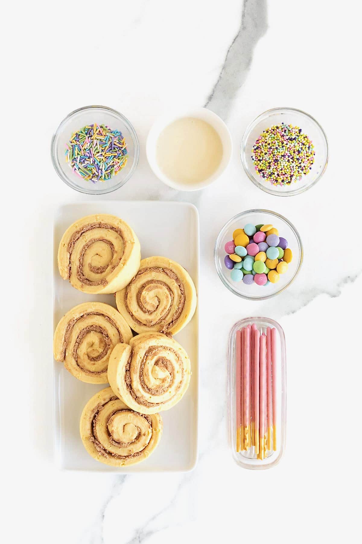 Ingredients to make butterfly shaped cinnamon rolls in small dishes on a white marble counter.